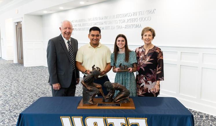 Two males and females standing in front of a table with a navy ETBU tablecloth and Jesus feet washing statue on the top of the table